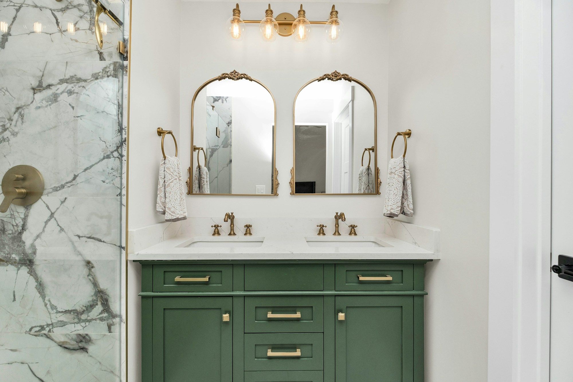 Green double vanity with brass faucets and arched mirrors